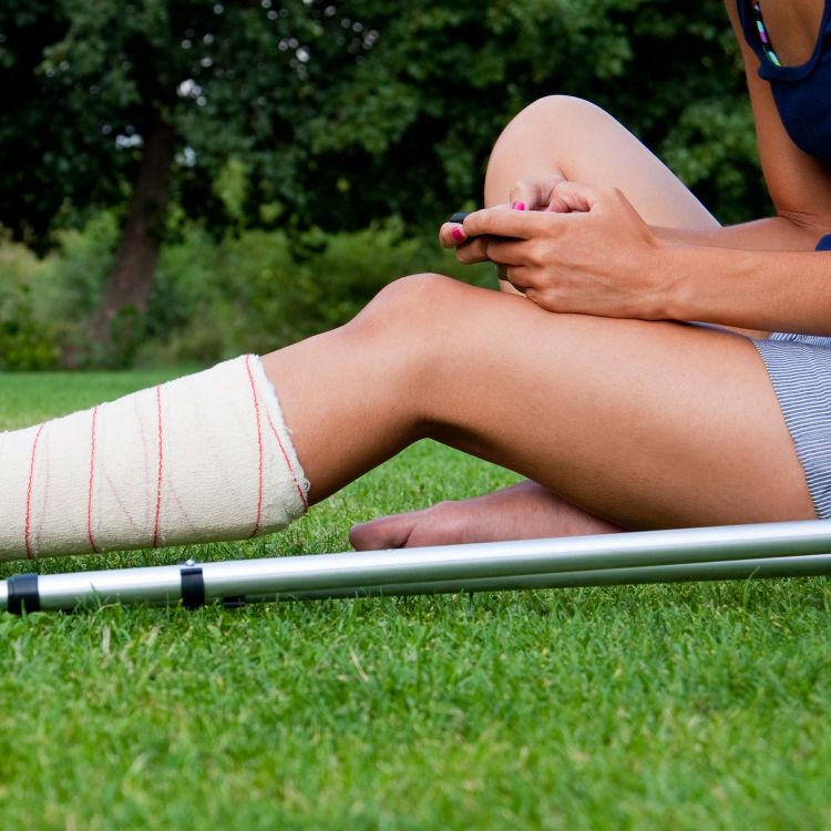 Jeune femme assise dans l'herbe avec une jambe dans le plâtre